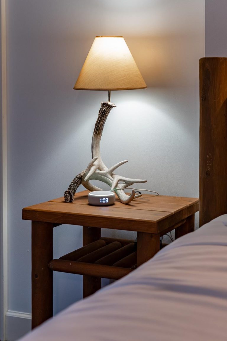 a table with a lamp on top of it next to a bed