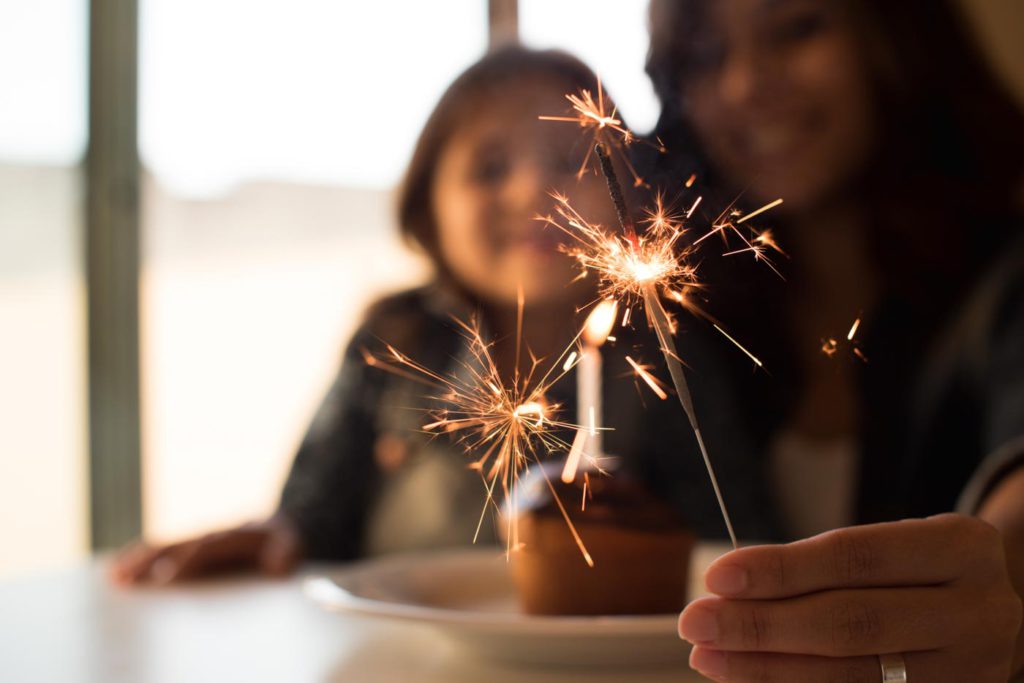 woman and her daughter holding a sparkler and blowing out birthday candles